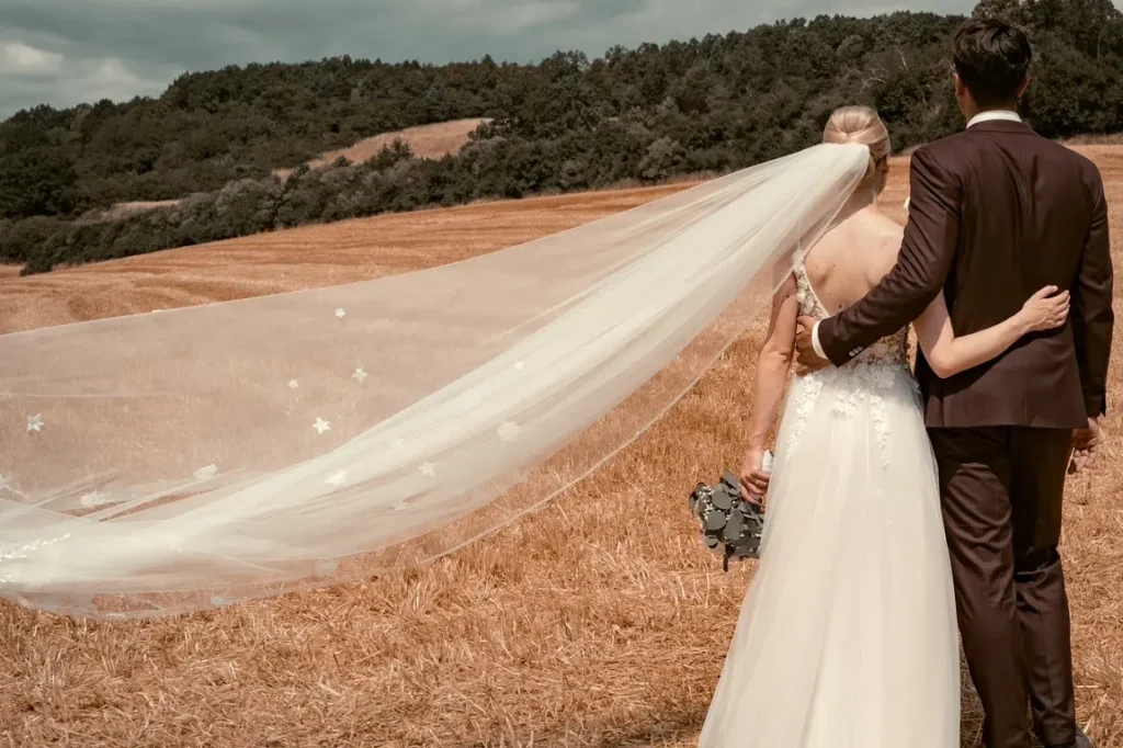 Braupaar umarmt sich und schaut auf das Feld vor ihnen. Der Schleier der Braut wird im Wind getragen. Fotografiert von hochzeitsfotograf-bamberg.net