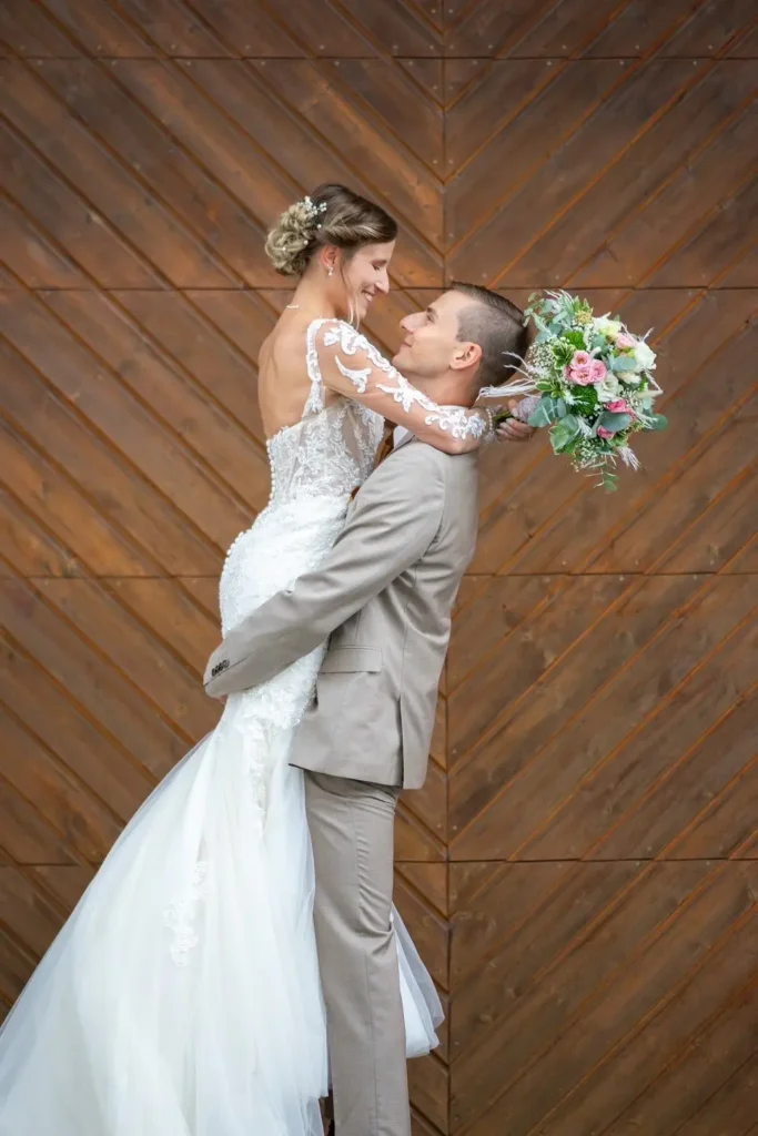 Bräutigam hebt die Braut hoch und schaut ihr ins Gesicht. Braut hält den Brautstrauß hinter dem Kopf des Bräutigams. Fotografiert von hochzeitsfotograf-bamberg.net