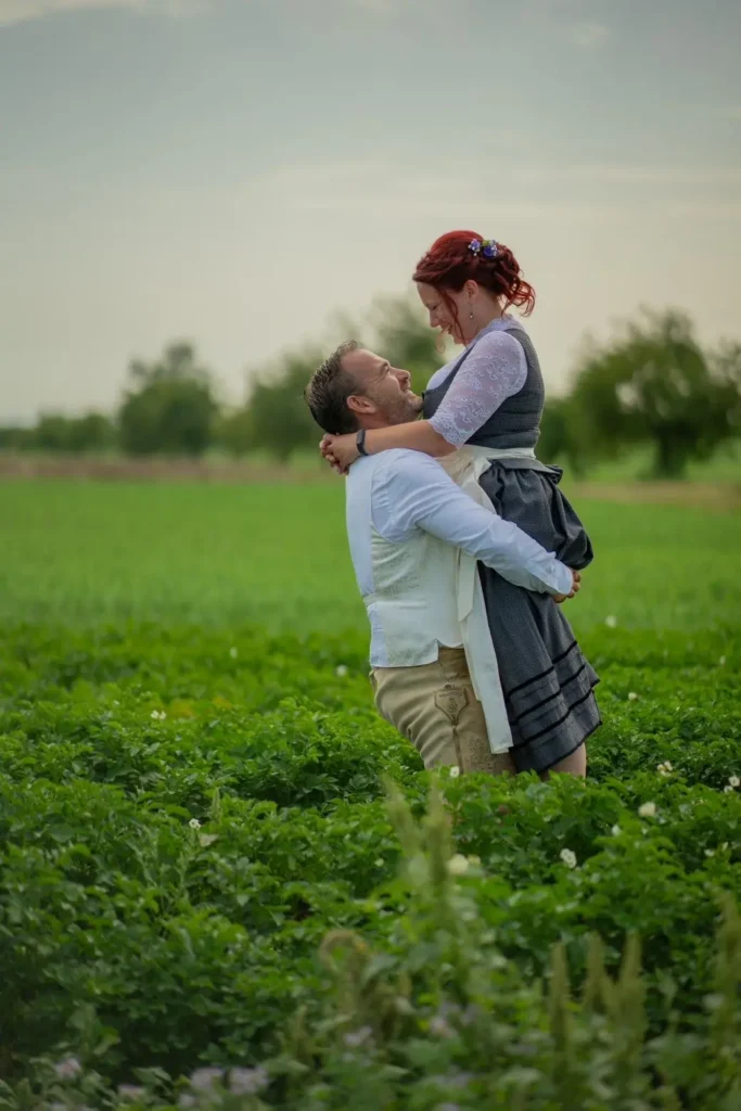 Brautpaar steht im grünen Feld. Bräutigam hält die Braut hoch. Das Brautpaar ist in Trachtenkleidung gekleidet. Fotografiert von hochzeitsfotograf-bamberg.net