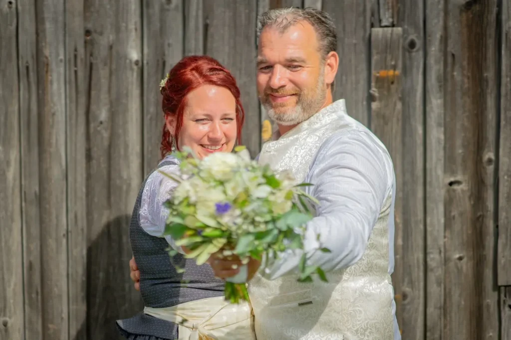 Brautpaar umarmt sich. Braut und Bräutigam strecken jeweils mit einem Arm den Hochzeitsstrauß in die Kamera. Fotografiert von hochzeitsfotograf-bamberg.net