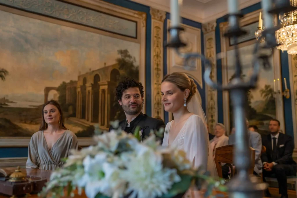 Brautpaar sitzt im Standesamt Coburg vor der Standesbeamtin. Die Trauzeugin sitzt neben dem Bräutigam. Der Bräutigam schaut verliebt die Braut an. Fotografiert von hochzeitsfotograf-bamberg.net