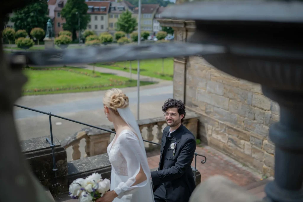 Braut in weißem Kleid hält den Brautstrauß in der linken Hand. Mit der rechten Hand zieht sie den Bräutigam hinter sich her. Dieser schaut sie lächelnd an. Fotografiert von hochzeitsfotograf-bamberg.net