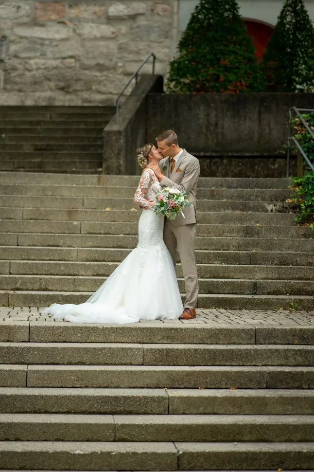Brautpaar steht auf einer steinernen Treppe und küsst sich. Fotografiert von hochzeitsfotograf-bamberg.net