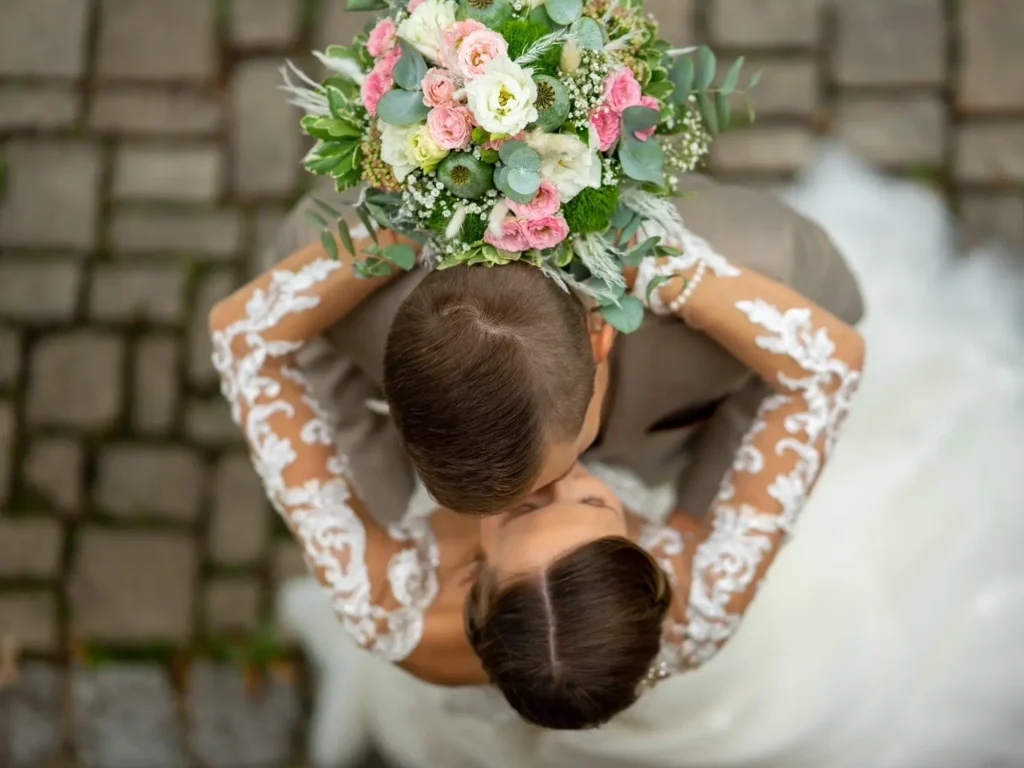 Braut umarmt den Bräutigam und hält dabei den Blumenstrauß hinter seinem Kopf. Bräutigam umarmt die Braut an der Hüfte. Von oben Fotografiert. Man sieht die Köpfe und den Blumenstrauß scharf. Fotografiert von hochzeitsfotograf-bamberg.net