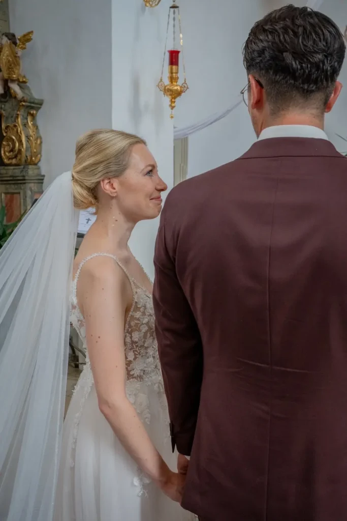 Braut und Bräutigam stehen vor dem Altar. Braut lächelt mit Tränen in den Augen den Bräutigam an. Fotografiert von hochzeitsfotograf-bamberg.net